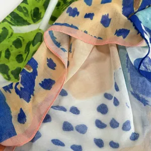 Close-up detail of artistic printed square scarf, showing soft fabric texture and colorful pattern.