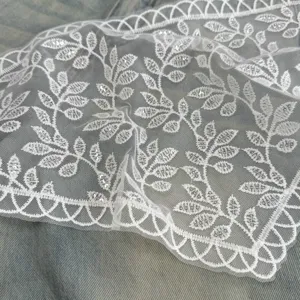 Close-up detail of delicate white lace fabric featuring embroidered leaves and shimmering sequins.