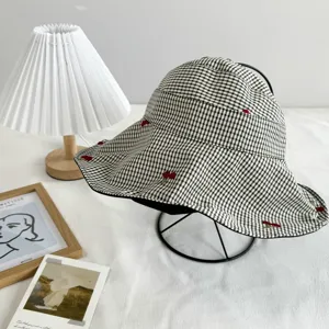 Black and white plaid bucket hat with cute red cherry embroidery, stylish sun protection.