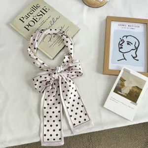 Vue détaillée d'un long foulard en soie rose à pois noirs et perles, ruban élégant pour cheveux.