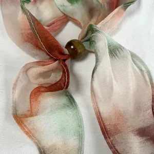 Elegant silk scarf detail view showcasing delicate tie-dye watercolor pattern with chic beaded closure.