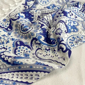 Detailed close-up view of blue and white paisley print triangle scarf with delicate white fringe.
