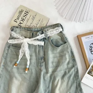 Vaqueros de mezclilla clara combinados con un elegante cinturón de cinta de encaje blanco y borlas.
