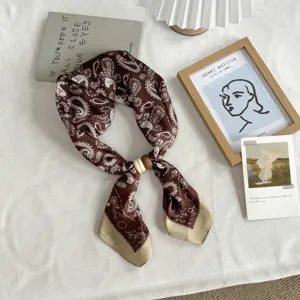 Detailed view of brown paisley silk scarf with wooden ring accessory on white fabric.