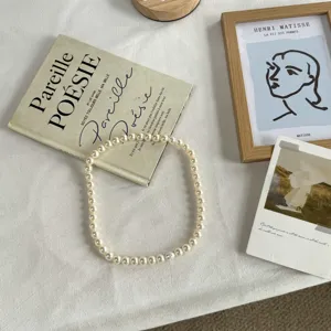 Gros plan de detail du collier de perles rondes elegantes sur fond de tissu blanc, style epure.