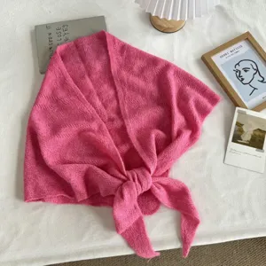 Gros plan sur un foulard triangulaire en tricot rose douillet, texture douce et nouage à l'avant.