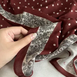 Detailed view of women's burgundy polka dot cashmere-feel square scarf with paisley border.