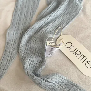 Detailopname van lichtblauwe ajour gebreide driehoekige sjaal met textuur en label.