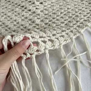 Détail en gros plan du tissu en résille crochetée blanc cassé avec bordure frangée.