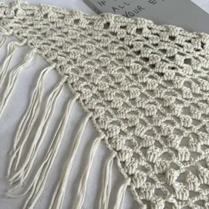 Gros plan d'un foulard triangulaire en dentelle crochetée beige avec franges détaillées.