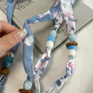 Detailed view of women's decorative silk scarf necklace with colorful beads and fabric ribbon design.