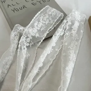 White lace ribbon scarf detail showing delicate floral embroidery and soft mesh fabric.