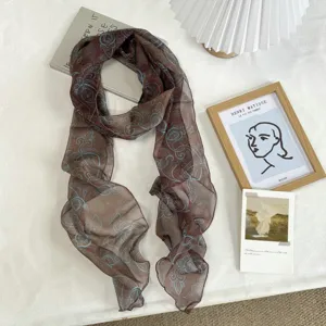 Detailed view of a brown gradient long silk scarf with blue paisley pattern on white table.