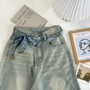 Detailed close-up of light wash denim jeans with a chic blue paisley print ribbon and bead belt.