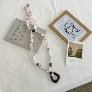Detailopname van de bloemige sjaalketting met houten ringhanger en kleurrijke kralen.