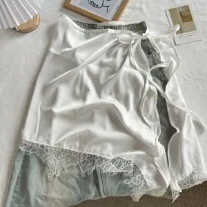Witte satijnen wikkelrok met kanten rand gelaagd op denim jeans, modieus kledingstuk.
