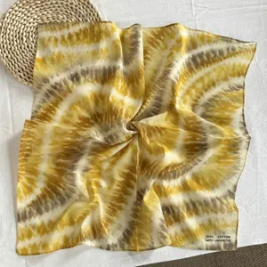 Vista dettagliata di un foulard quadrato in puro cotone con motivo tie-dye giallo e grigio.