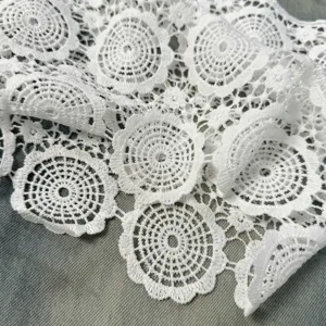 Close-up detail of white lace fabric trim with hollow round flower patterns, fine texture.