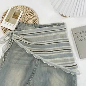 Jupe portefeuille transparente rayée chic superposée à un jean, accessoire de taille asymétrique.
