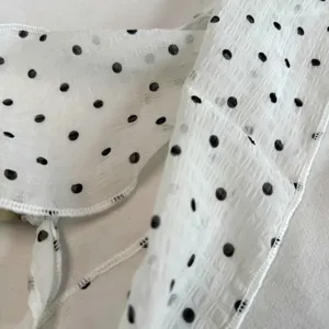 Detailed close-up of white sheer polka dot neck scarf fabric texture with fine stitched edges.