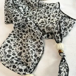 Details of black and white floral long scarf with beads, soft fabric, elegant neck accessory.