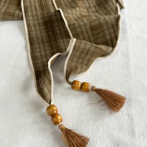 Detailansicht des braunen Karomuster-Dreiecktuchs mit Holzlöchern, Perlen und Quasten.
