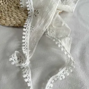 Detail van witte kanten bloemendriehoeksjaal, delicate pomponrand en elegante striklintjes.