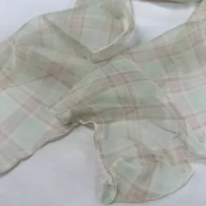Close-up detail van een pastelgroene en roze geruite chiffon sjaal met golvende rand.