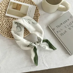 Close-up detail of white and green floral print silk square scarf neckerchief flat lay.