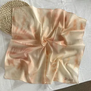 Dettaglio in primo piano di foulard quadrato in cotone puro con toni arancioni e crema.