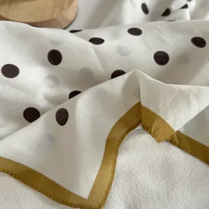 Petit carré de soie en coton blanc à pois noirs avec bordure jaune, gros plan texture.