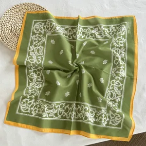 Gedetailleerd overzicht van een groene katoenen paisley bandana met witte print en gele rand.