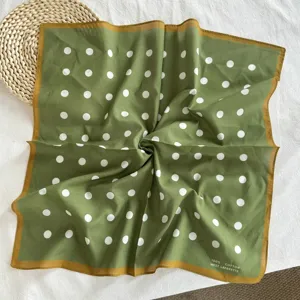Vue détaillée d'un petit carré de soie en coton vert à pois avec bordure contrastée.