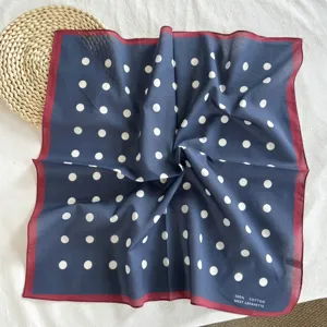 Détail en gros plan du foulard carré classique en coton bleu marine à pois et bord rouge.