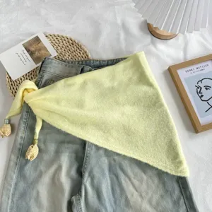 Detail shot of a stylish yellow knitted triangular scarf with plaid tassel pendants styled on denim.