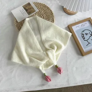 Close-up view of a creamy white knit triangular scarf featuring red plaid tulip pendants.