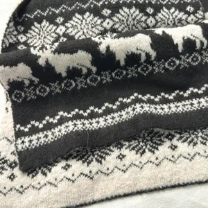Close-up detail of cozy black and white knit scarf featuring winter reindeer and snowflake pattern.