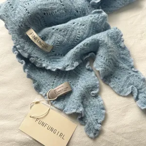 Gros plan sur les details du foulard triangulaire en tricot bleu clair, texture douce.