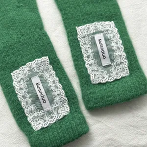 Green knitted long gloves detail showcasing soft textured fabric and elegant white lace patch.