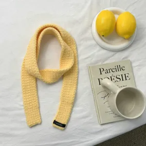 Close-up detail view of a cozy yellow knitted narrow scarf with a small black brand label.