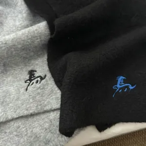 Close-up detail view of soft knit winter scarf featuring delicate embroidered logo texture.