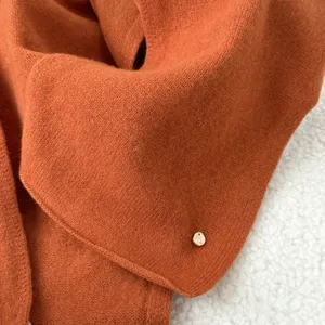 Cozy orange knit scarf detail close-up, soft wool texture, elegant metal charm accent for winter.
