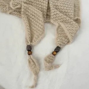 Gros plan détaillé du foulard triangulaire en résille beige avec élégantes perles en bois.