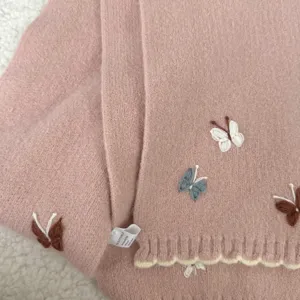 Detalle de bufanda de punto rosa con bonito bordado de mariposa y dobladillo festoneado.
