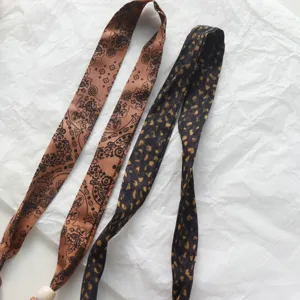 Fabric ribbon necklace detail shot, elegant printed silk-like scarf with bead accessory.