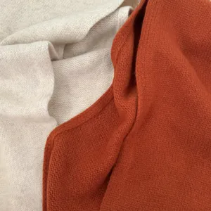 Close-up detail view of soft knit wool scarf fabric in cream and rust orange colors.