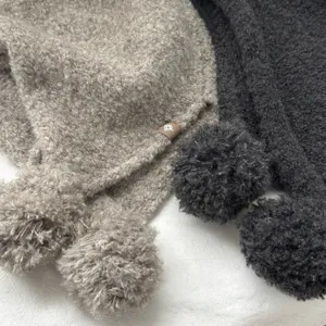 Close-up detail of cozy wool winter balaclava hat with fluffy pom-poms and cute logo.