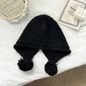 Close-up detail of black knitted balaclava hat with fluffy pom-poms, cozy texture.