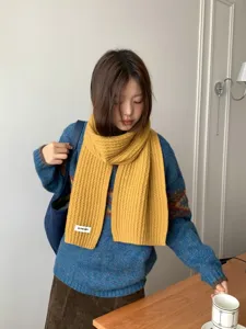 Detail view of a cozy yellow knitted winter scarf worn by a model in a warm indoor setting.