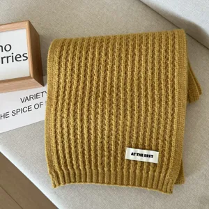 Detailed view of a soft yellow knitted winter scarf with ribbed texture and woven label.